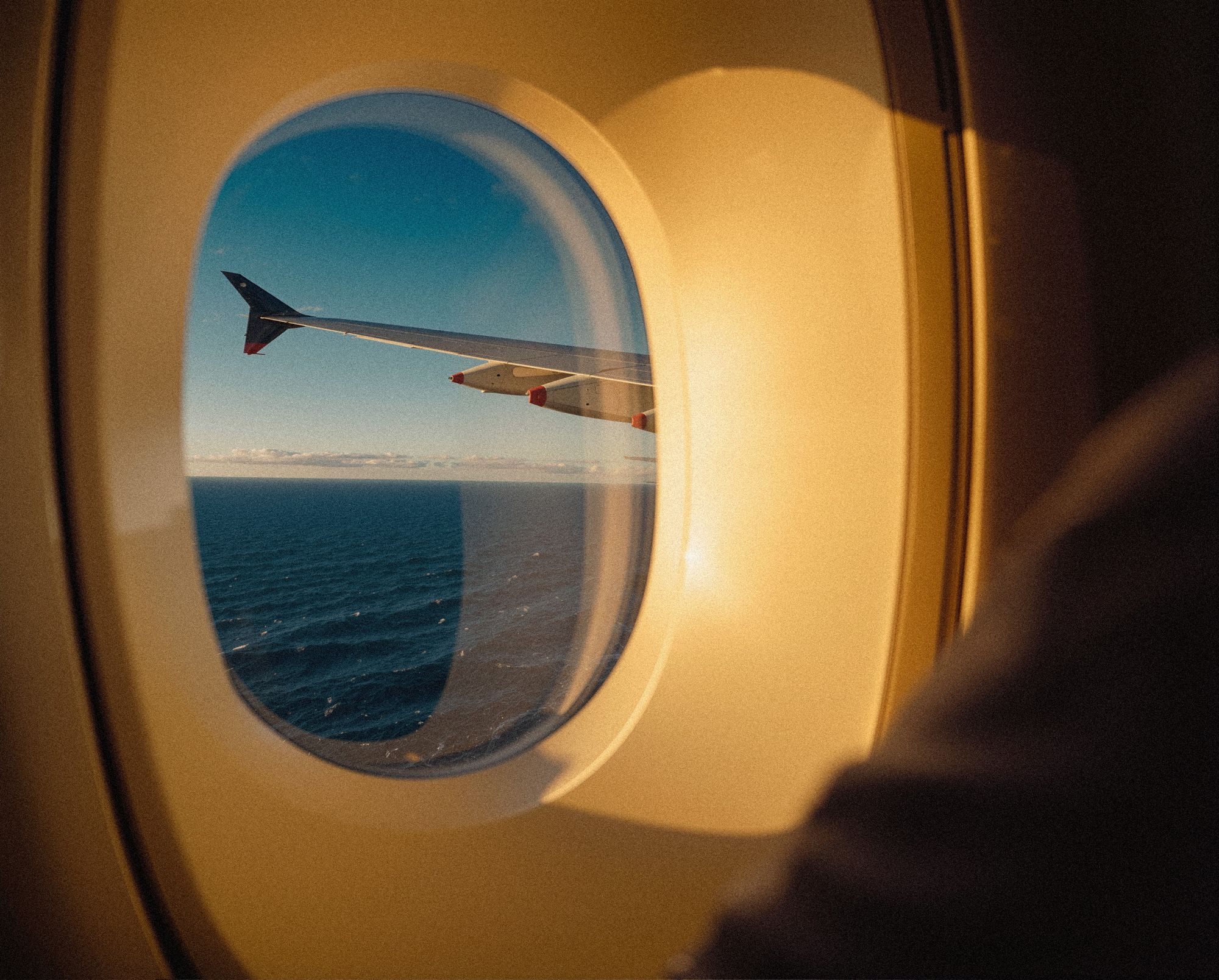 View of an airplane wing over the ocean through a cabin window at golden hour